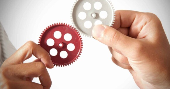 Two different people holding up mechanical gears that work together.