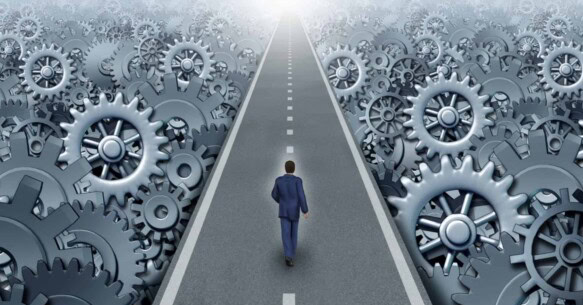 A business person walks down a road toward the horizon surrounded by working gears.