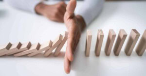 The hand of a business person blocks the domino effect.