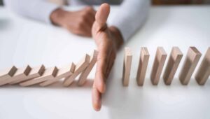 The hand of a business person blocks the domino effect.