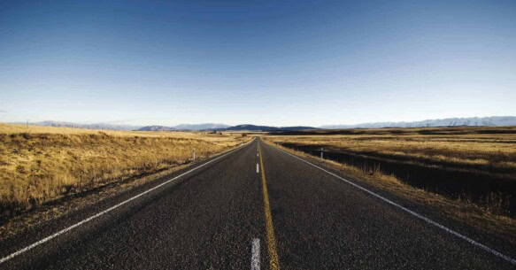 A highway stretches through an open field towards the horizon