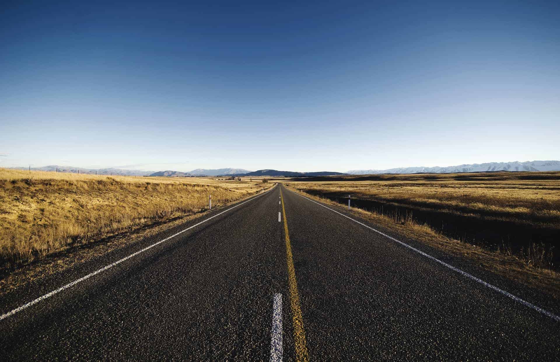 A highway stretches through an open field towards the horizon