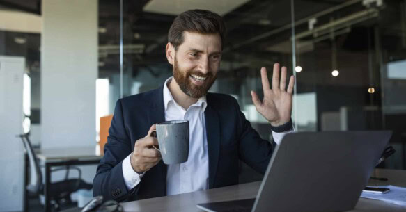 Smiling middle aged businessman waving hand at laptop webcamera, having meeting in office interior, free space